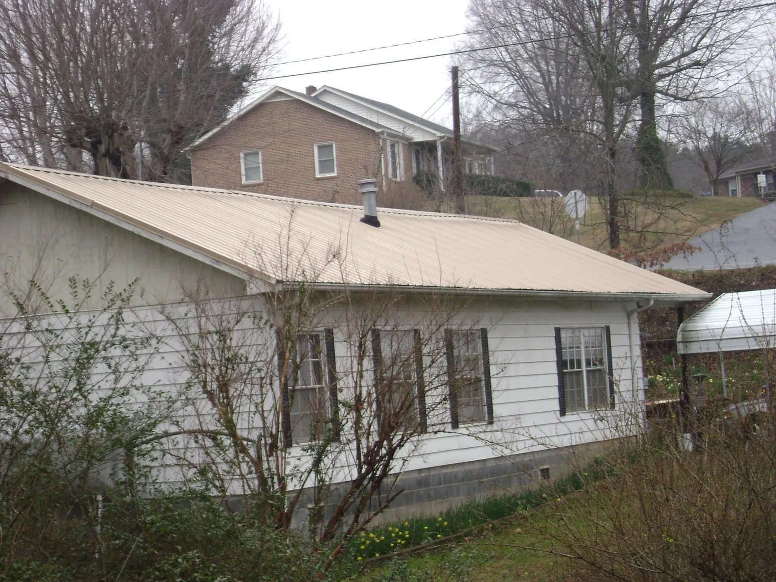 Tan metal roof on a white sided house set into a hillside — Commercial Roofing by Roofing Brothers in Ennis
