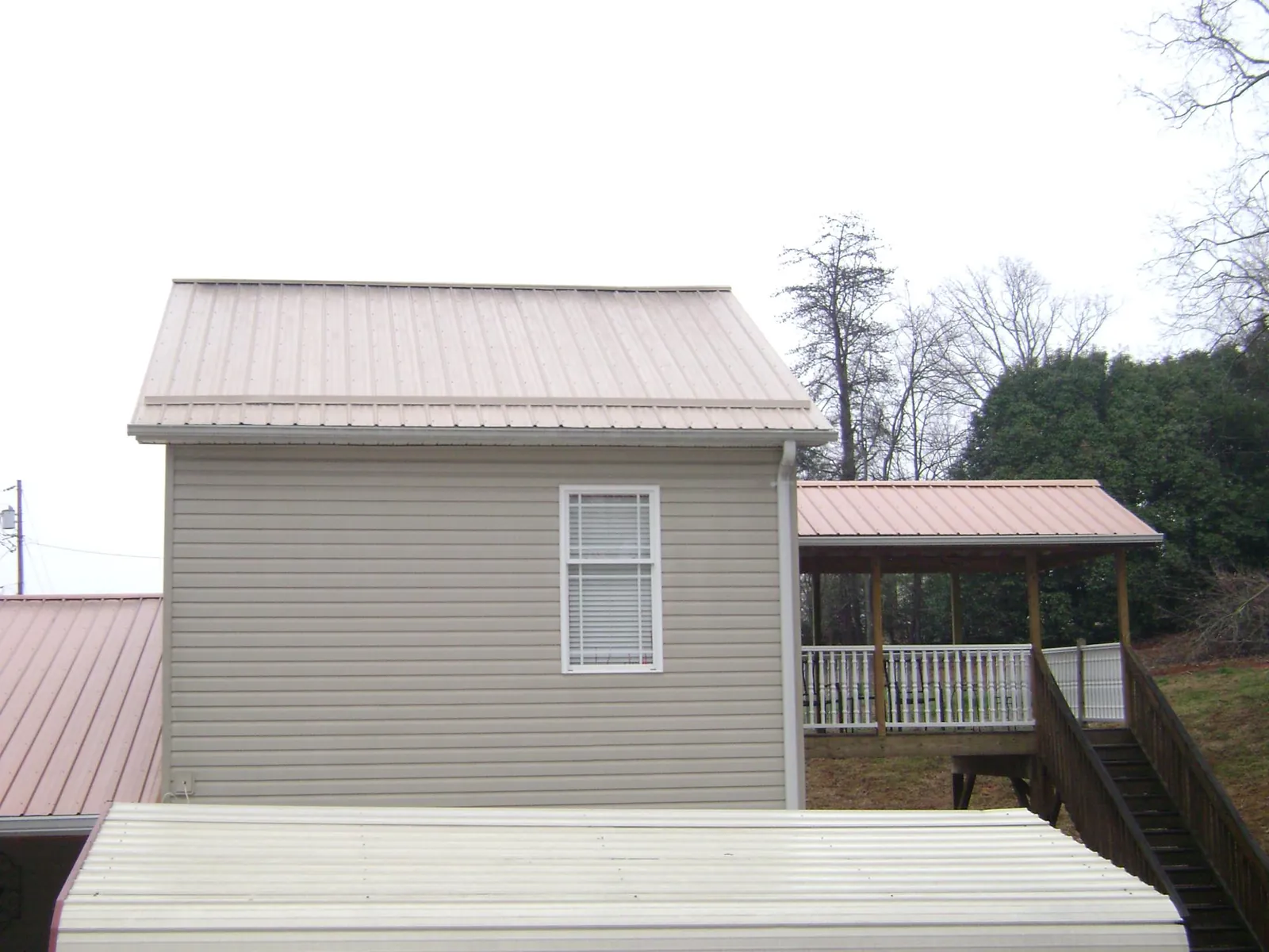 Tan metal roofs on a two story addition and attached porch, from a Roof Replacement job in Ennis